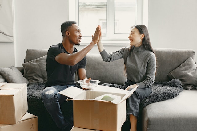 people sitting on a couch high fiving while unpacking a box